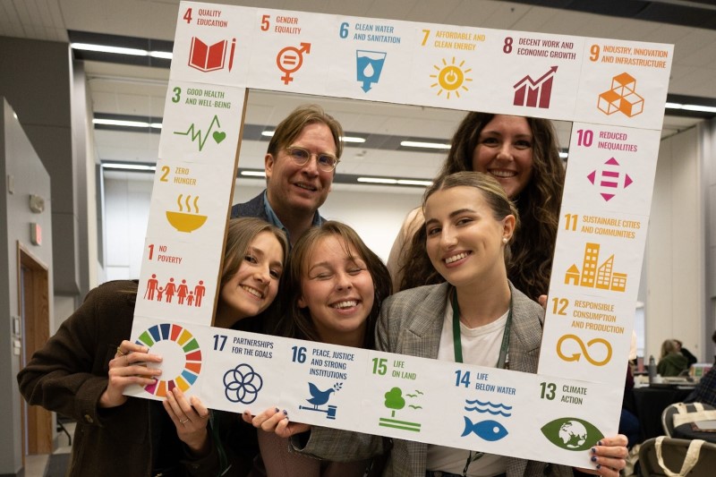 The sustainability team poses with their heads in a frame decorated with SDG icons