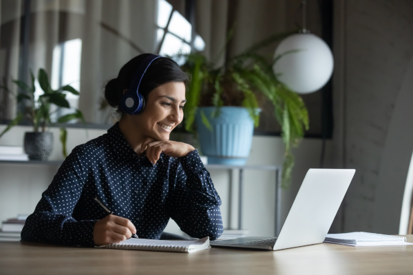 Happy young woman with headphones looking at laptop screen.