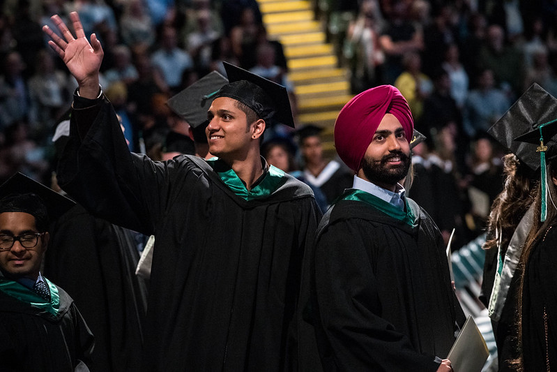 Two young graduates, smiling and waving at Convocation.