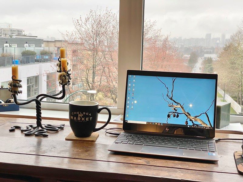 A laptop is open on a table with a cup of tea and a nice view out the window.