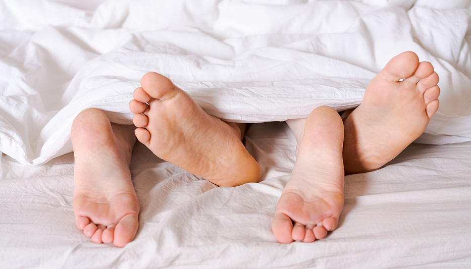 2 pairs of feet poking out from under the sheets